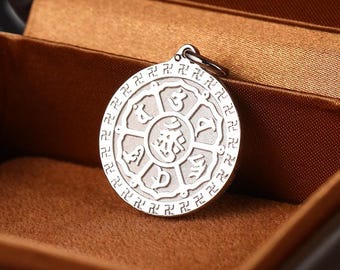 May include: A circular silver-toned metal pendant featuring an embossed eight-spoked wheel design with central script characters and a border pattern of repeating swastika symbols. The pendant includes a small metal jump ring at the top.