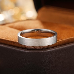 Könnte beinhalten: Ein silberfarbener Metallring mit flacher, gebürsteter Oberfläche und einem schlichten, schmucklosen Banddesign. Der Ring weist eine glatte, matte Textur auf der Außenseite auf und zeigt eine klare, kreisförmige Form mit gleichmäßiger Breite.