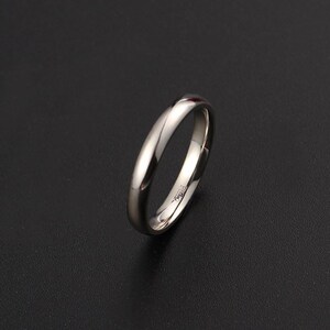 May include: A polished, silver-colored ring with a smooth, rounded band. The ring is set against a dark background, highlighting its reflective surface. The ring appears to be a wedding band or a simple, elegant piece of jewelry.