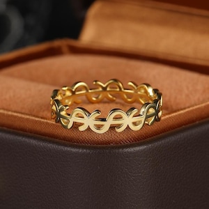 May include: A gold-toned ring featuring a continuous band design composed of repeating dollar sign symbols. The metal has a polished finish, and the openwork structure creates a series of interconnected, stylized currency motifs around the entire circumference.
