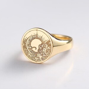 Könnte beinhalten: Goldener Siegelring mit eingraviertem Design von Sonne, Mond und Wolken. Der Ring hat eine polierte Oberfläche und eine abgerundete Oberfläche. Der Ring mit Himmelsmotiv ist ein stilvolles Accessoire. Der Durchmesser beträgt ca. 2,5 cm.