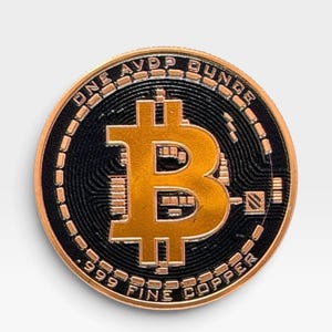 Puede incluir: Una moneda redonda de color cobre con un símbolo de Bitcoin prominente en el centro. El texto dice ONE AVP OUNCE en la parte superior y 999 FINE COPPER en la parte inferior. El fondo de la moneda tiene un patrón negro de circuito.