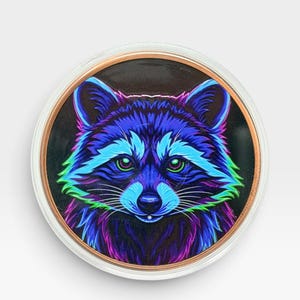 May include: A circular pin featuring a stylized raccoon illustration with vibrant neon blue, purple, and green fur highlights against a dark background. The raccoon has bright green eyes and a black nose, enclosed within a metallic copper-toned rim.