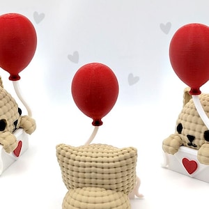 以下が含まれることがあります： ベージュ色のテディベアの置物が3つ。それぞれ白い封筒と赤いハート、赤い風船を持っています。風船は白い紐でクマに繋がれています。背景は白で、小さな灰色のハートの形が描かれています。