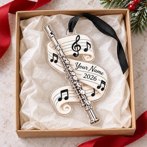 Peut inclure: Une décoration en acrylique transparent représentant une flûte argentée superposée à un ruban blanc orné de notes de musique noires, d'une clé de sol et du texte Your Name et 2026. L'ornement est fixé à un ruban noir pour la suspension.
