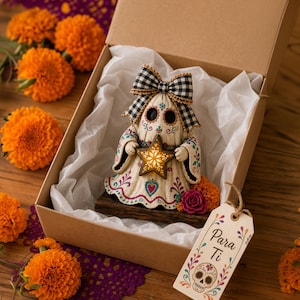 May include: A cream-colored ghost figurine with colorful floral patterns, a black and white checkered bow, and a glowing star in its hands. It sits in a cardboard box with white tissue paper and a tag that reads Para Ti with a skull illustration.