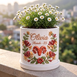 May include: White ceramic planter with a floral design and the name "Olivia" and the date "March-25". The planter features a red ram symbol and is filled with daisies.