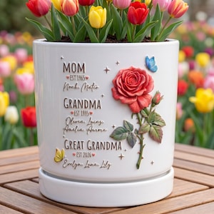 May include: White ceramic flower pot with a red rose and butterfly accents. The pot is inscribed with the words "MOM," "GRANDMA," and "GREAT GRANDMA," along with names and dates. The pot is filled with colorful tulips.