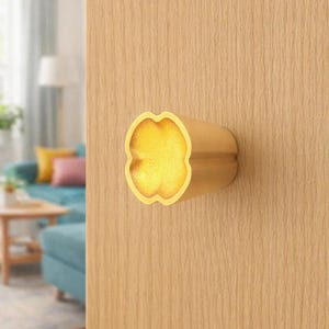 May include: A gold-colored door knob with a four-leaf clover design. The knob is cylindrical with a rounded, textured surface. The door is made of light-colored wood.