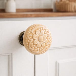 以下が含まれることがあります： ベージュ色の装飾的なキャビネットノブ。 浮き彫りの花柄のデザイン。 ノブは、暗いブロンズ色のベースに取り付けられ、白いキャビネットドアに取り付けられています。 キッチンやバスルームの家具に最適です。