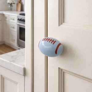 Könnte beinhalten: Hellblauer Schrankknauf in Form eines Footballs mit roten Streifen. Der Knauf ist an einer weißen Schranktür befestigt. Dieser dekorative Knauf verleiht Küchen- oder Badezimmermöbeln eine sportliche Note.
