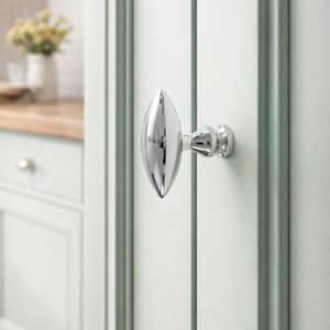 以下が含まれることがあります： 楕円形のデザインの、磨かれたクロム製のドアノブ。 ドアノブは、垂直パネルのある淡い緑色のドアに取り付けられています。 背景には、白いキャビネットと木製のカウンタートップを備えたキッチンの様子が映っています。