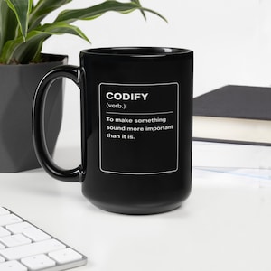 Peut inclure: Un mug noir avec l'inscription blanche "CODIFY" et sa définition : "Rendre quelque chose plus important qu'il ne l'est".