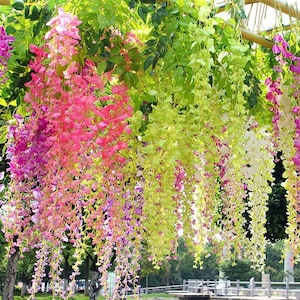 May include: A vibrant display of artificial wisteria flowers in shades of pink, purple, yellow, and white. The cascading blooms are suspended from a green leafy canopy, creating a colorful and decorative floral arrangement.
