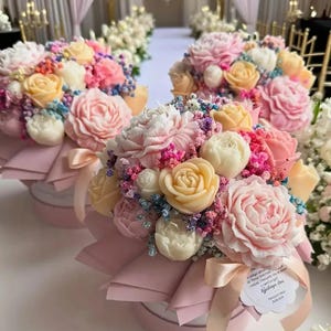 Puede incluir: Arreglos florales con rosas, peonías y otras flores en tonos pastel. Los ramos están dispuestos en cajas redondas rosas y atados con cintas rosas. Las flores son de color rosa, blanco y amarillo, creando un ambiente romántico.