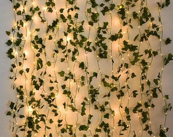 May include: A wall of decorative string lights with artificial green ivy leaves. The lights are small and warm-toned, creating a soft glow. The ivy is arranged in a cascading pattern, adding a natural touch to the decor.