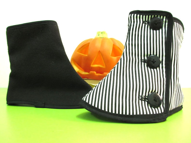 May include: Two Halloween-themed boot covers. One is solid black, the other is black and white striped with three large black buttons. An orange carved pumpkin is in the background. The boot covers are on a green surface.