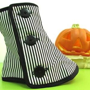 May include: A black and white striped bootie with three large black buttons. The bootie has a black trim and is next to an orange jack-o'-lantern. The bootie is likely a Halloween or costume accessory.