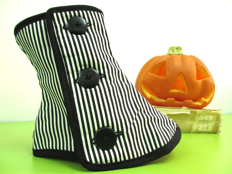 May include: A black and white striped bootie with three large black buttons. The bootie has a black trim and is next to an orange jack-o'-lantern. The bootie is likely a Halloween or costume accessory.
