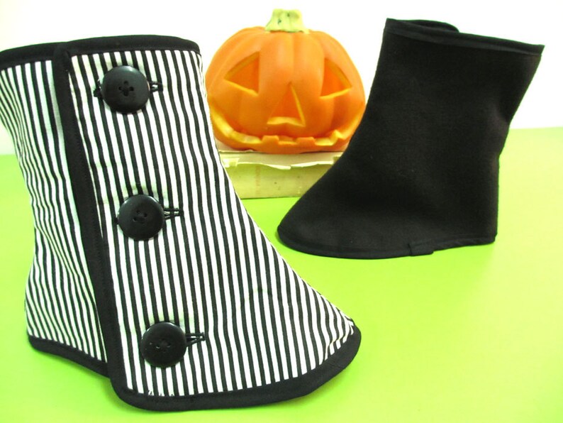 May include: Two decorative boot covers, one black and white striped with black buttons, the other solid black. A carved orange pumpkin sits in the background. The boot covers are likely for Halloween or costume use.
