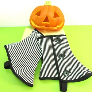 May include: Black and white striped fabric arm cuffs with black trim and three black buttons. A carved orange pumpkin sits in the background, suggesting a Halloween theme.