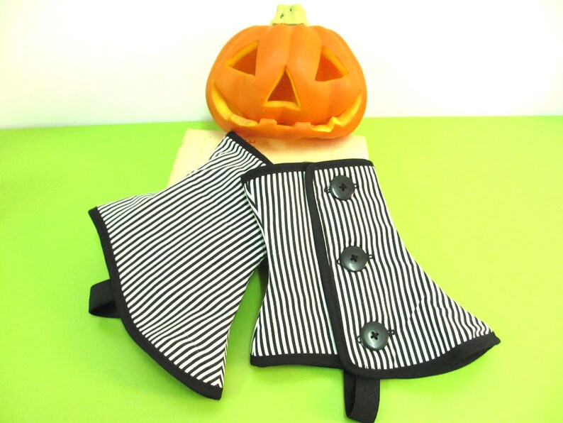 May include: Black and white striped fabric arm cuffs with black trim and three black buttons. A carved orange pumpkin sits in the background, suggesting a Halloween theme.