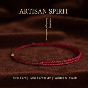 May include: A thin, deep red braided thread cord bracelet featuring a small gold-toned bead. The text ARTISAN SPIRIT, Gathering Blessings Good Fortune, and Thread Cord | 1.5mm Cord Width | Colorfast & Durable are visible in the image.