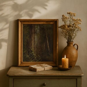 May include: A framed landscape painting with a wooden frame, depicting a forest scene with tall trees and sunlight. A stack of aged paper tied with twine, a lit candle, and a brown vase with dried flowers sit on a weathered wooden table.