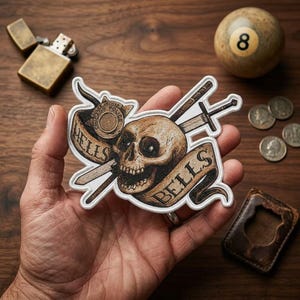 May include: A detailed sticker featuring a skull with crossed swords and a banner reading "HELLS BELLS". The design includes a Chicago Police badge. A vintage lighter, an 8-ball, and coins are also visible.