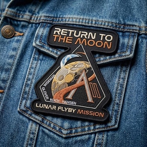 May include: A black and orange embroidered patch with the text "RETURN TO THE MOON" and "LUNAR FLYBY MISSION" on a denim jacket. The patch features a stylized moon, a triangle, and the names "WISEMAN", "GLOVER", "KOCH", and "HANSEN".