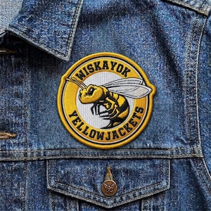 May include: A circular embroidered patch with the text "WISKAYOK YELLOWJACKETS" in yellow and black. The patch features a yellow and black cartoon wasp with white wings, sewn onto a blue denim jacket.