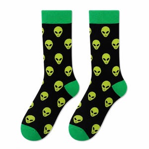 May include: A pair of black crew socks featuring a repeating pattern of lime green alien heads. The socks have solid lime green cuffs, heels, and toes, providing a distinct contrast against the black fabric and the bright green extraterrestrial motifs.