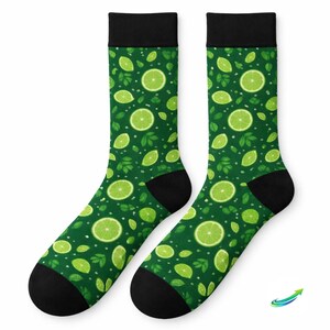 Könnte beinhalten: Ein Paar grüne Socken mit einem Muster aus Limettenscheiben und Blättern. Die Socken haben schwarze Fersen und Zehen sowie schwarze Bänder oben. Der Hintergrund ist dunkelgrün.