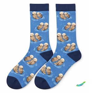 Peut inclure: Paire de chaussettes bleues avec un motif d'otaries flottant dans l'eau. Les chaussettes ont des talons, des orteils et des poignets bleu marine. Les loutres sont marron et blanches, et l'eau est bleu clair avec des reflets blancs.