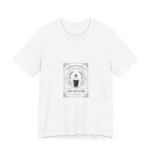 Puede incluir: Camiseta blanca con un gráfico de una botella de poción con el texto "Luna Sage Elixir" y "Nightshade Crystal Apothecary". El diseño está en un marco rectangular con elementos botánicos.