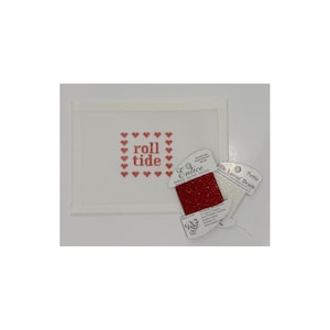 May include: A white needlepoint canvas with the words "roll tide" stitched in red, surrounded by red hearts. Two spools of thread are next to the canvas, one red and one white. The red thread is labeled "Entice".