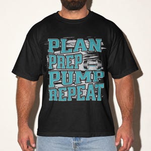 以下が含まれることがあります： 黒の半袖Tシャツ。ブロック体で書かれたティール色の「PLAN PREP PUMP REPEAT」というテキストが積み重なっている。グレーのダンベルのグラフィックがデザインに組み込まれており、かすれたグレーの長方形の背景要素の上に配置されている。