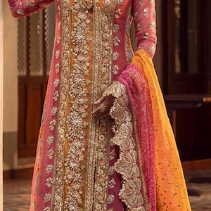 May include: A long-sleeved pink and orange dress featuring intricate gold embroidery, beadwork, and sequins. The garment includes a sheer pink overlay with a scalloped border, a deep V-neckline, and a matching orange skirt with horizontal gold stripes.