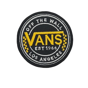 Può includere: Toppa rotonda nera con il logo Vans giallo. La toppa ha un bordo bianco con la scritta "OFF THE WALL" in alto e "LOS ANGELES" in basso. È visibile anche la scritta "EST 1966".