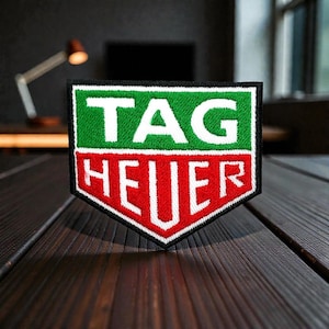 May include: Embroidered patch featuring the TAG HEUER logo. The patch has a green top section with the word "TAG" in white, and a red bottom section with "HEUER" in white. The patch is bordered in black.