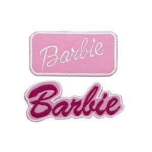 May include: Two embroidered patches featuring the word "Barbie". One is rectangular with a pink background and white script. The other has a pink and magenta colour scheme with a cursive font.