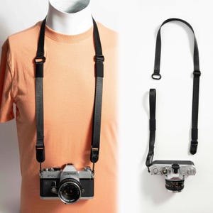 May include: A black adjustable camera strap made of durable nylon webbing, featuring quick-release connectors. The strap is shown attached to a silver and black Canon FTb 35mm film camera, with a second view showing the detached strap.