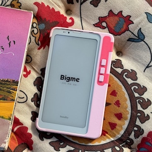 May include: A light pink e-reader device with a white screen displaying the text Bigme JUST FOR YOU and Standby. The device features a vertical row of three rectangular buttons on the right side and a light pink protective case frame.