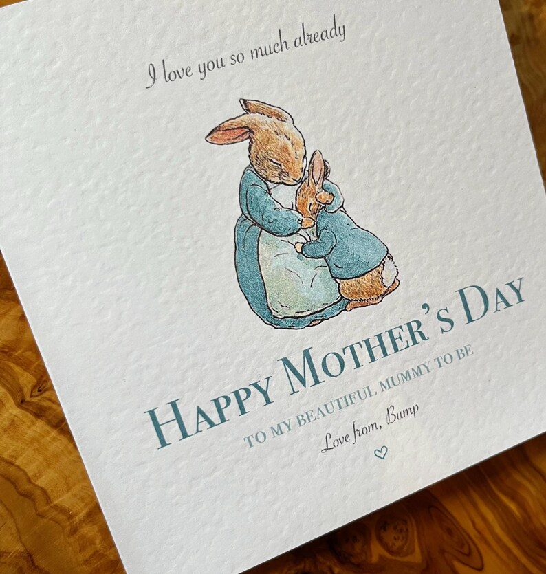 Pu&ograve; includere: Biglietto per la festa della mamma con un'illustrazione ad acquerello di due conigli che si abbracciano. Il biglietto recita "Happy Mother's Day" e include il testo "Ti amo gi&agrave; cos&igrave; tanto" e "Love from, Bump."
