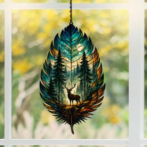 Könnte beinhalten: Dekorativer, blattförmiger Fensterhänger mit einer Waldszene. Das Bild zeigt einen Hirsch vor einem Wald, mit einem Vollmond im Hintergrund. Das Blatt ist teal, blau und orange und hängt an einer Kette.