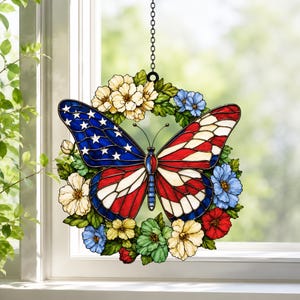 Könnte beinhalten: Ein Buntglas-Sonnenfänger mit einem zentralen Schmetterling, dessen Flügel in Rot, Weiß und Blau gemustert sind und an die amerikanische Flagge erinnern. Der Schmetterling ist von einem kreisförmigen Kranz aus bunten Blumen und grünen Blättern umgeben.