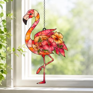 Pode incluir: Um apanhador de sol de vitral em forma de flamingo, com tons vibrantes de rosa, laranja e amarelo. O flamingo é adornado com padrões florais detalhados, incluindo flores de hibisco, e pendurado por uma corrente de metal preta.