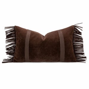 May include: A rectangular dark brown pillow featuring a soft, suede-like texture. The pillow is accented by two vertical smooth leather-like bands and long, thin fringe trim extending from both the left and right sides of the cushion.