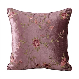 Può includere: Un cuscino quadrato in velluto malva con ricami floreali. Il design presenta una vite rampicante con rose e boccioli rosa e foglie verdi. Il cuscino ha un bordo viola scuro.