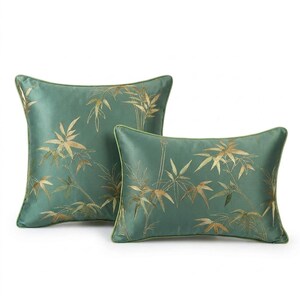 May include: Two decorative throw pillows in shades of teal green, featuring a gold bamboo leaf design. The pillows have a square and rectangular shape, with a matching green trim. The fabric has a slight sheen, giving it a luxurious appearance.